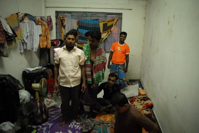 A group of migrant workers stand in a cramped and crowded room