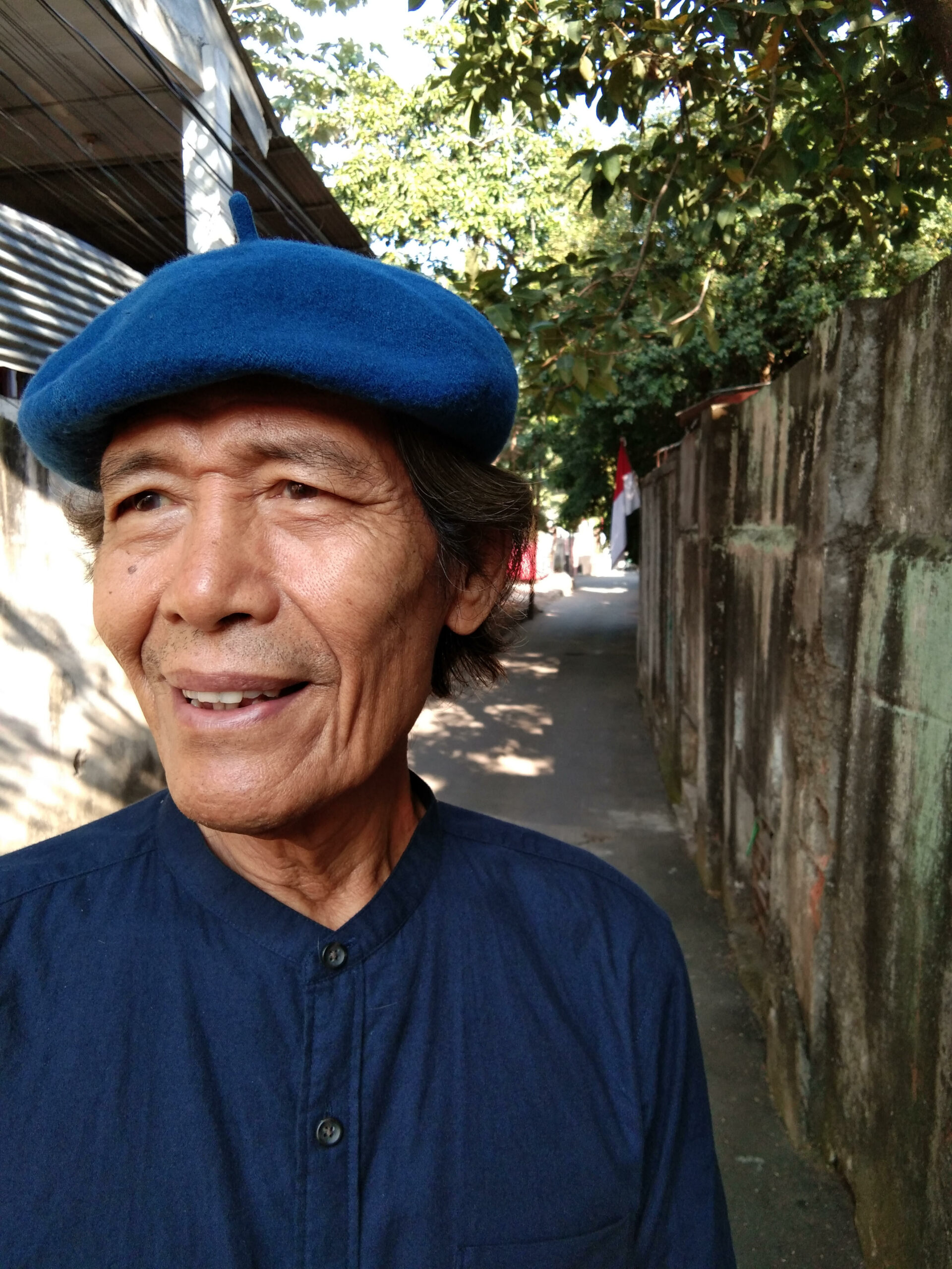 Martin Aleida wearing a blue beret, standing in an alleyway in Jakarta - New Naratif