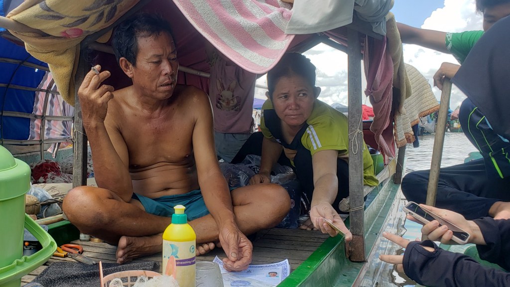 An ethnic Vietnamese couple aboard their fishing boat on the Mekong River near the Cambodia-Vietnam border show reporters their IDs and other documents in July 2021.