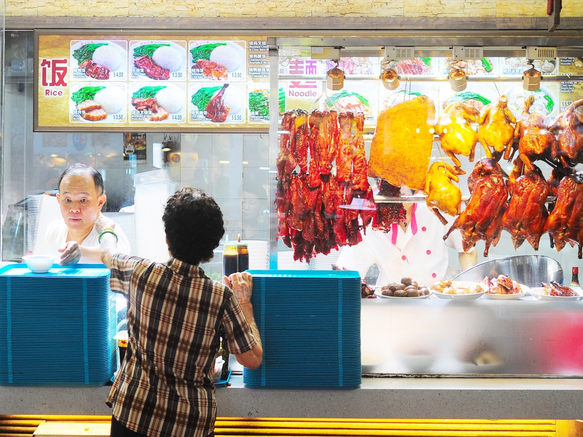 A male hawker interacts with a woman standing at a food stall counter in Singapore. joyfull/Shutterstock